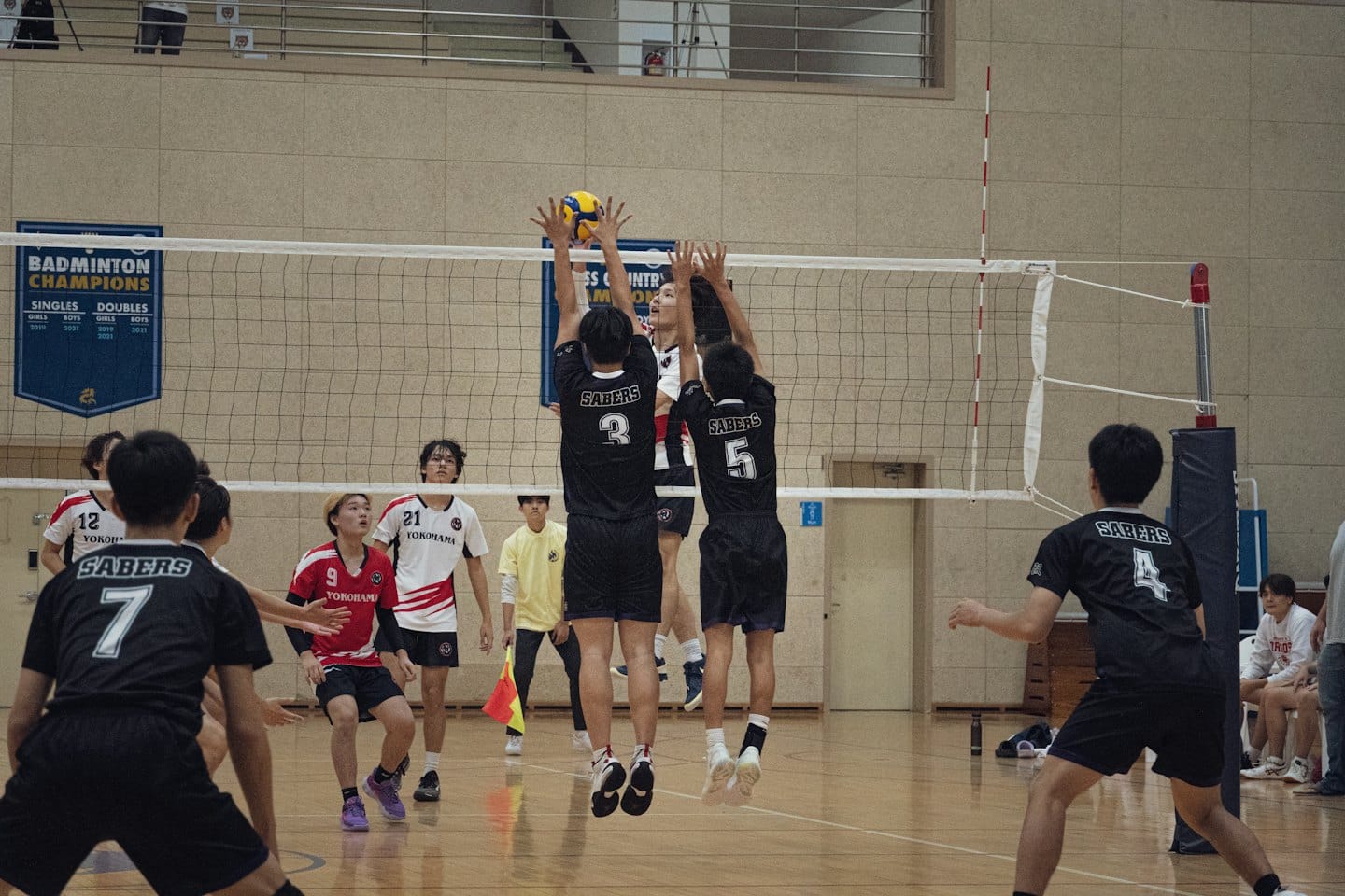Volleyballspieler springen in einer Sporthalle, um den Ball zu blocken.