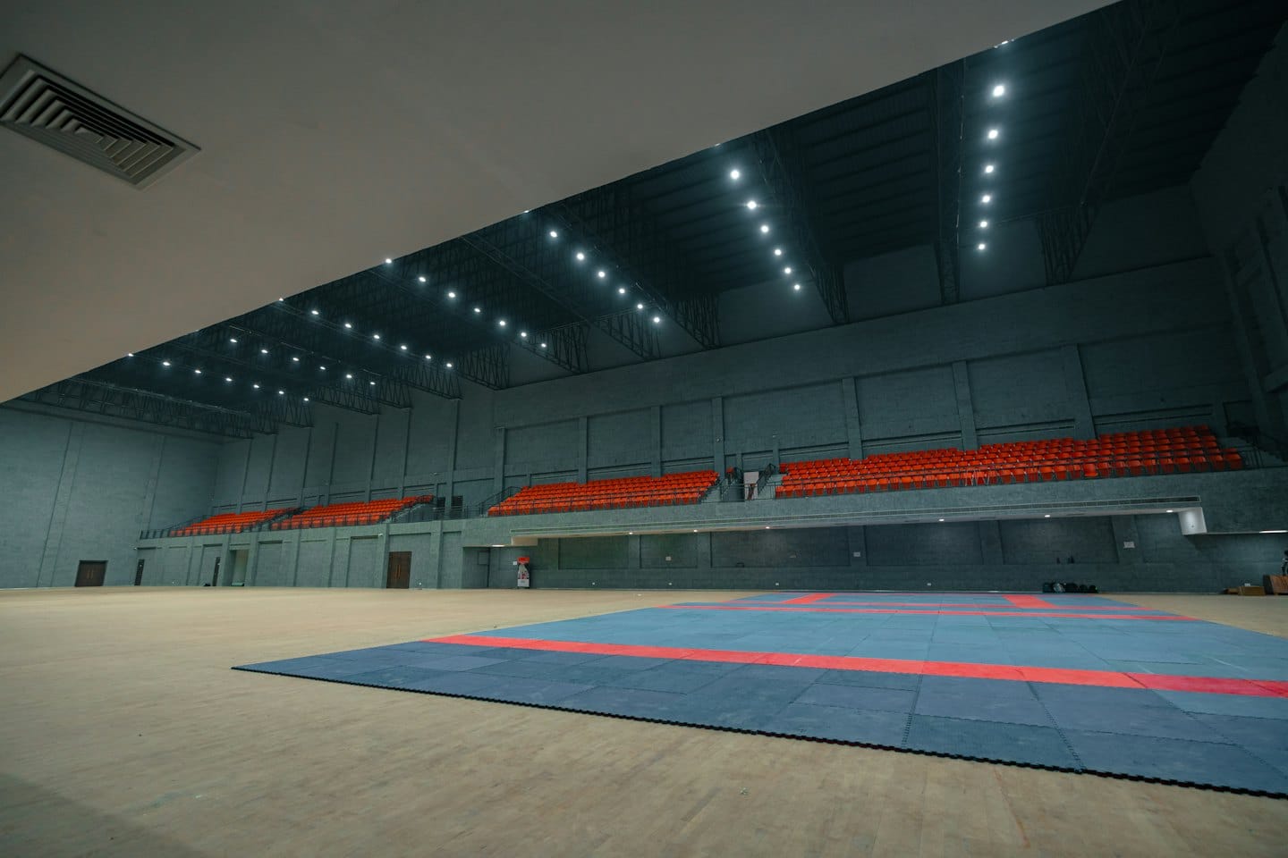 Leere Sporthalle mit Reihen roter Tribünensitze.
